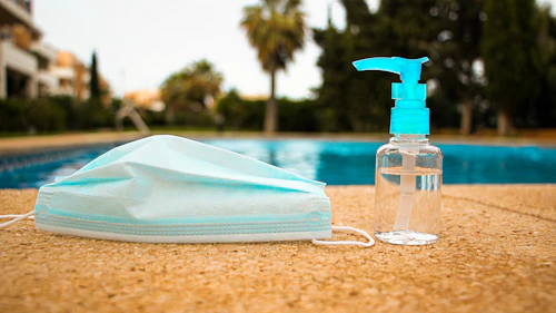 COVID-19 hand sanitizer and mask by a pool